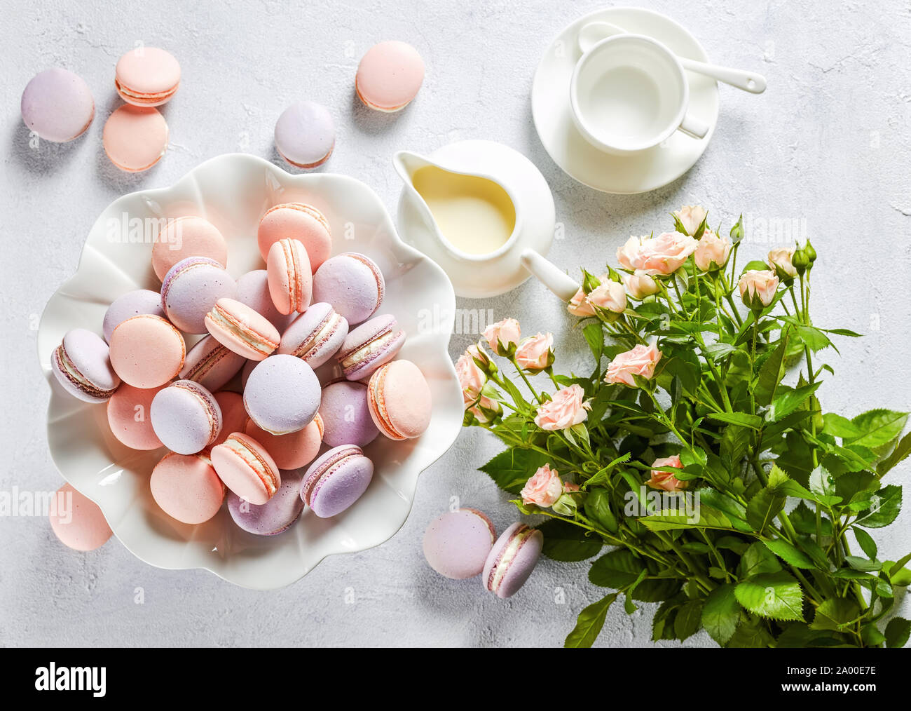 Französische macarons auf einem Porzellan Kuchen stehen und einige auf einer konkreten Tabelle mit Strauß mit frischen Blumen und Rahmtopf, horizontale Ansicht, Flach, close-up Stockfoto