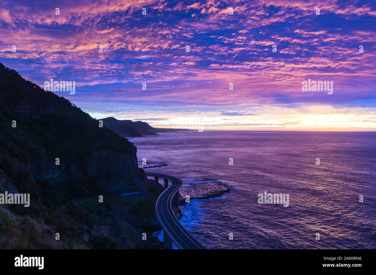 Sea Cliff Brücke auf sunrise mit schönen rosa und lila, violett Himmel und Meer im Hintergrund. Die Brücke ist Teil der Grand Pacific Highway Stockfoto