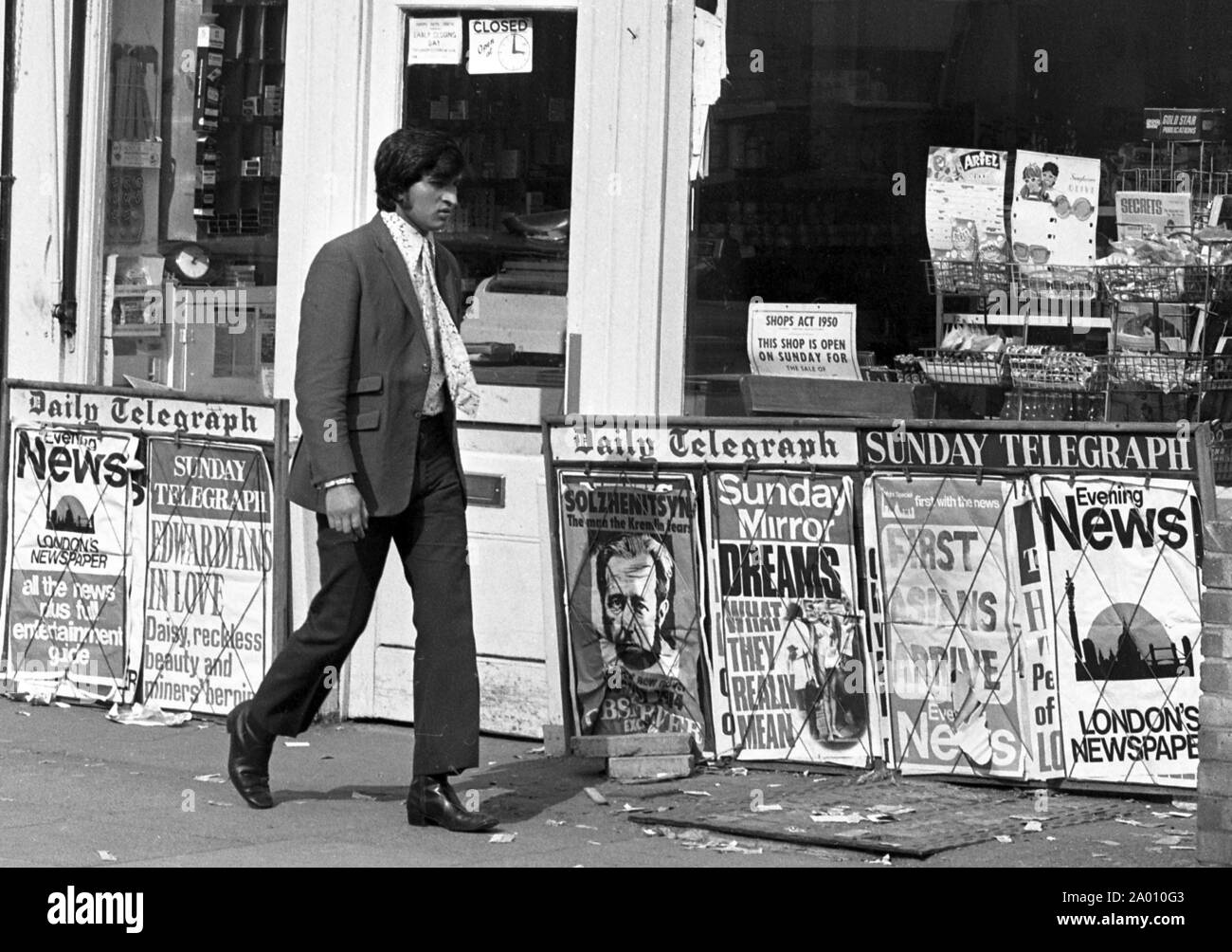 Southall, London 1972. Eine elegant gekleidete junge Inder vorbei gehen. Ein zeitschriftenladen mit Zeitung Werbung einen, "Erste Asiaten anreisen..". Nach Idi Amin bestellt 30.000 Asiaten aus Uganda mit 90 Tagen, die mit britischen Pässen zu England geleitet. Sie wurden gezwungen, ihr Geld, Eigentum und Besitz hinter sich zu lassen. Diese Bilder dokumentieren das Leben für einige der Menschen, wie sie in Southall, westlich von London nieder. Einen Einblick in das Leben vor 47 Jahren für Einwanderer in Großbritannien. Foto von Tony Henshaw Stockfoto