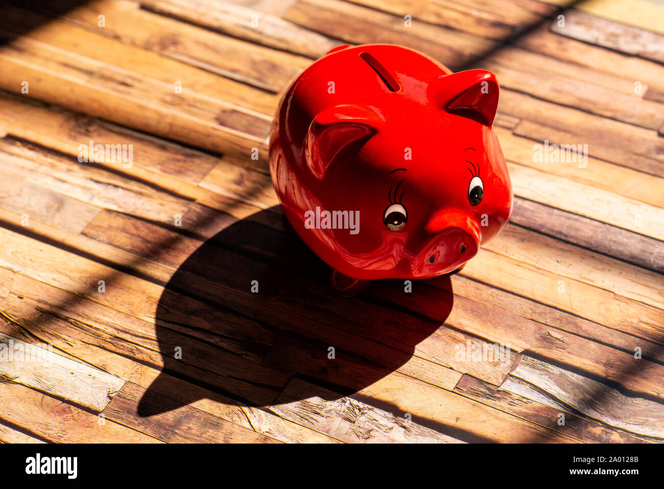 Ein rotes Sparschwein steht auf einem Holzboden und wirft einen starken Schatten Stockfoto