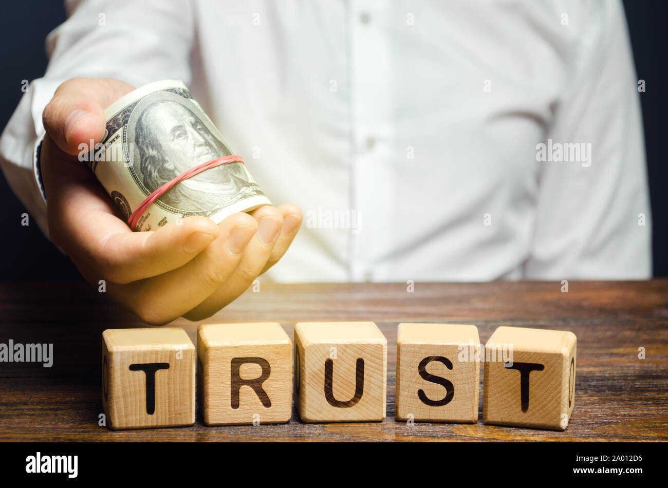 Holzblöcke mit dem Wort Vertrauen und Geld in die Hände eines Unternehmers. Vertrauensstellungen zwischen Geschäftspartnern, Freunden, Verwandten. Achtung Stockfoto