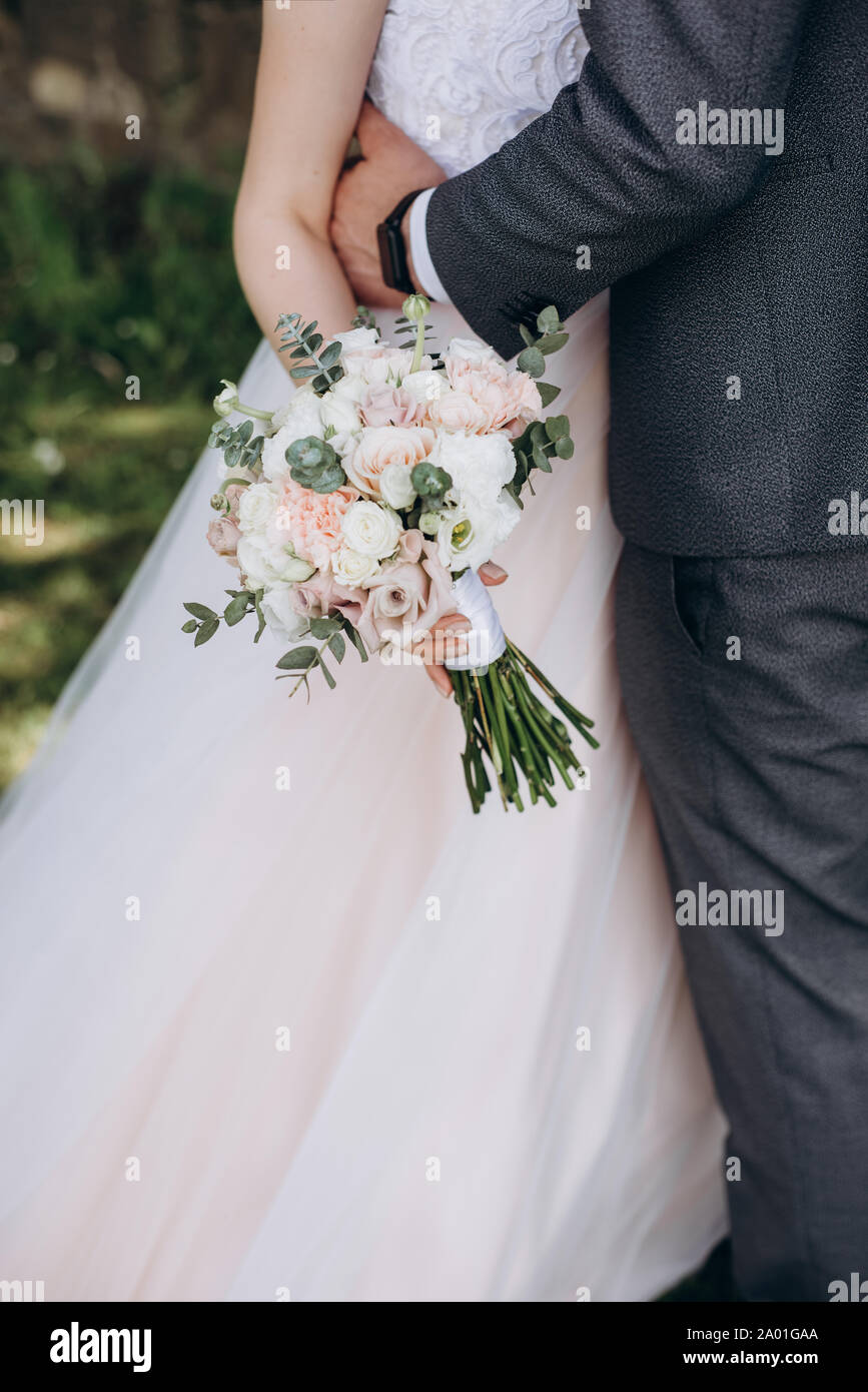 Nahaufnahme von Braut in einem weißen Kleid und ein Bräutigam in einem Anzug, umarmten und halten einen schönen Blumenstrauß von Weiß, rosa Blumen und Grün, eingerichtet. Stockfoto