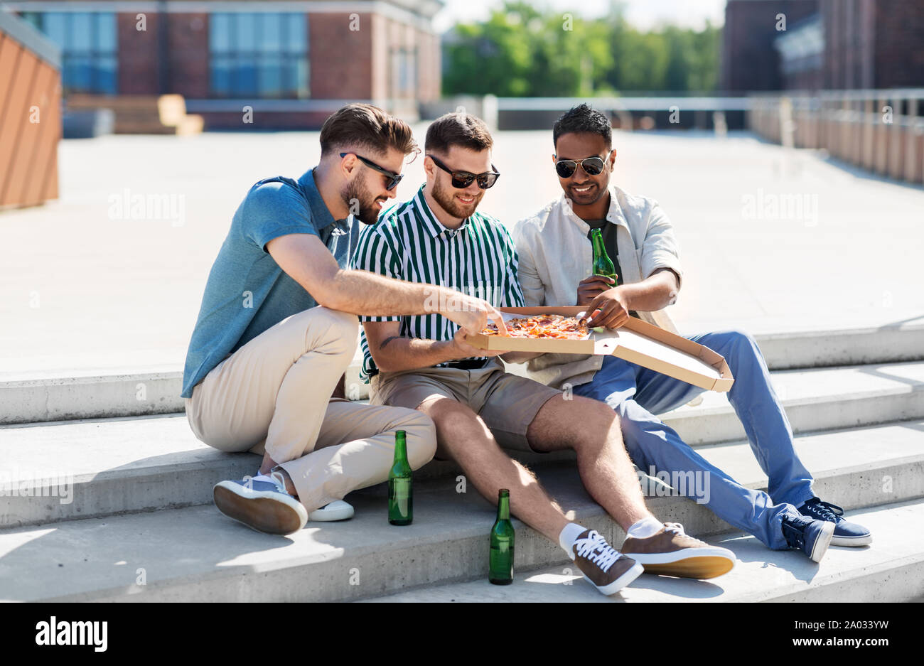 Männliche Freunde essen Pizza mit Bier auf der Straße Stockfoto