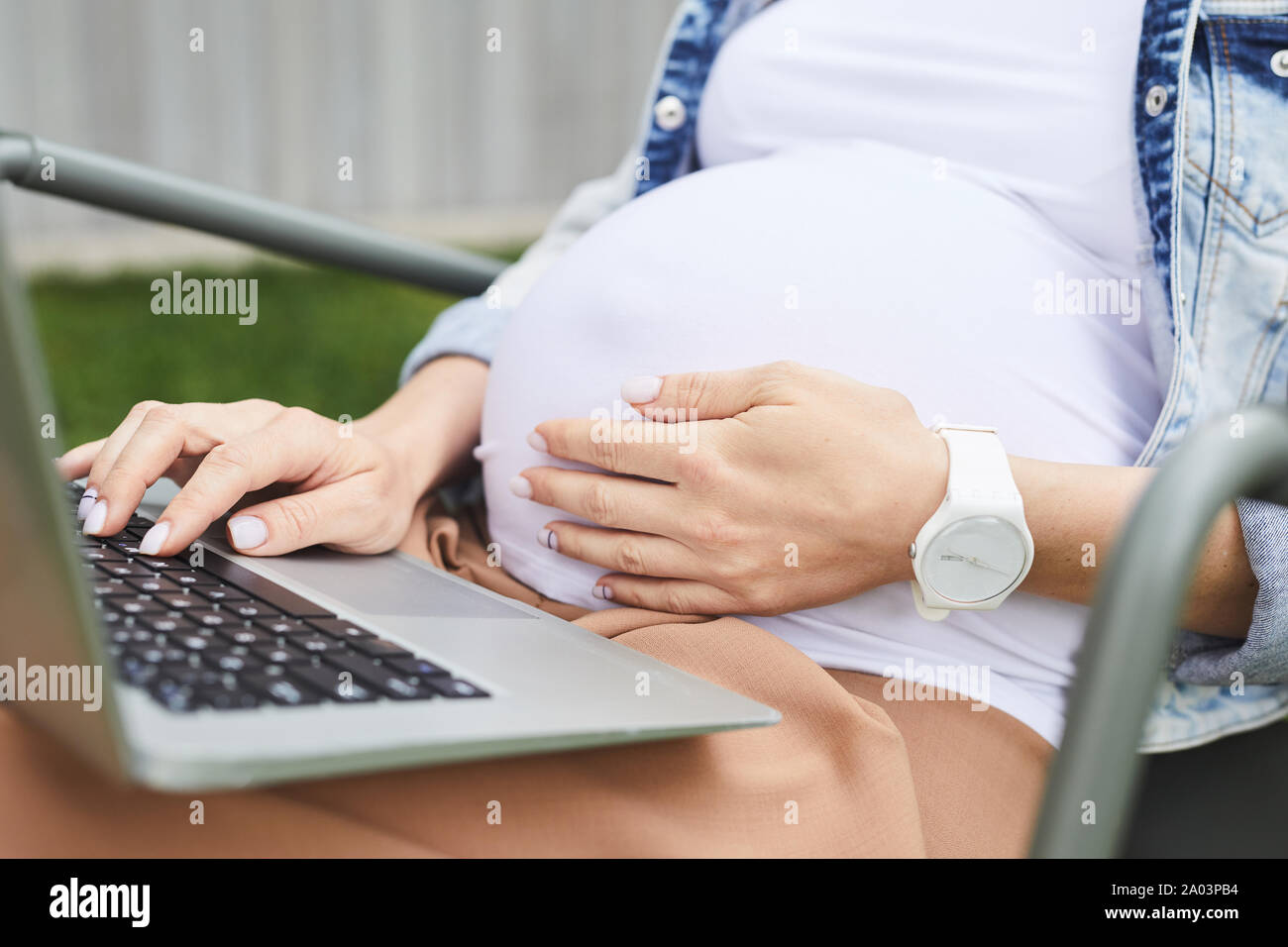 Nahaufnahme der schwangeren Frau, die ihren Bauch berühren beim Sitzen und mit Laptop im Freien Stockfoto