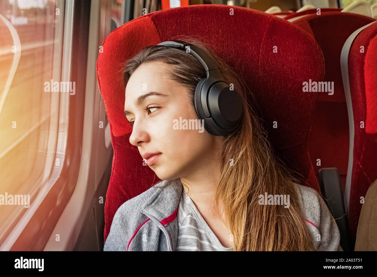 Junge Frau in Kopfhörer Musik hören über Kopfhörer und Suchen im Fenster des Zuges. Stockfoto