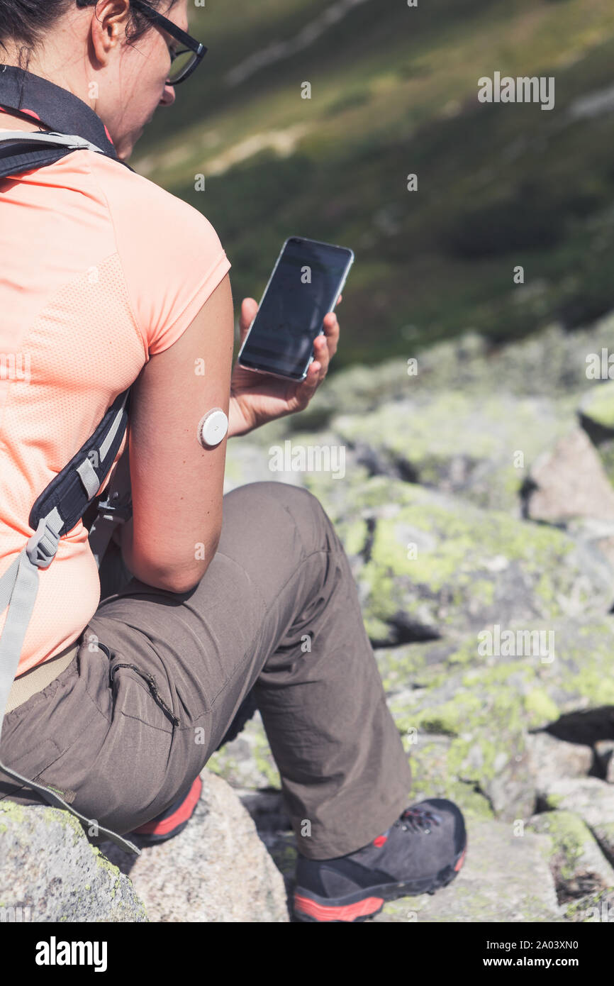 Das aktive Leben der Diabetiker, sitzt Frau am Handy mit überprüften Blutzuckerspiegel von neuer Technologie remote Sensor auf ihre Hand montiert auf der Suche Stockfoto