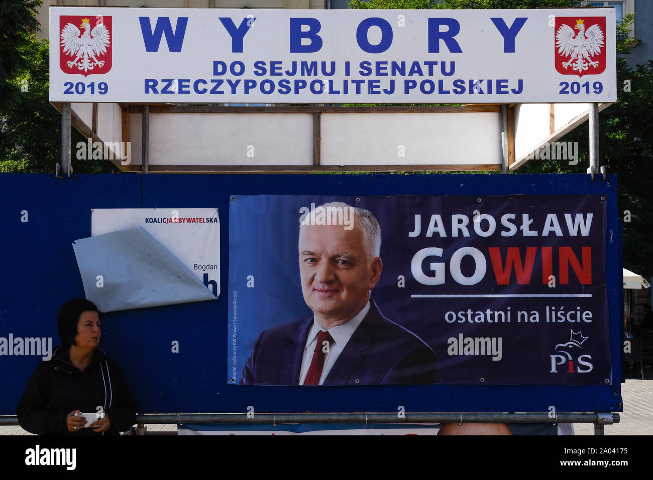 Eine Frau steht neben einem Wahlkampf Poster von Jaroslaw Gowin am Hauptplatz in Krakau. Die herrschende Regierung, Partei, Partei Recht und Gerechtigkeit mehrere neue soziale Wohlfahrt Pakete vor den Parlamentswahlen hat 500+' Kind Programm alle Kinder ausgedehnt hat angekündigt, eine Bonuszahlung für Rentner die Befreiung der Arbeiter unter 26 von der Einkommensteuer unter anderem. Stockfoto