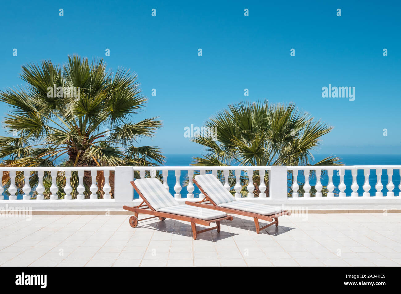 Sonnenliegen auf der Terrasse mit Blick aufs Meer und Palmen im Hintergrund Stockfoto