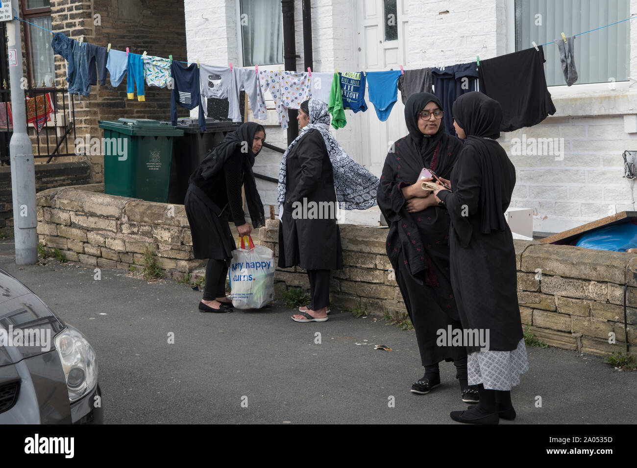 Muslimische Frauen Bradford Yorkshire 2019, 2010s Großbritannien. Frauen, die auf der Straße plaudern, tragen traditionelle schwarze Roben, die Abaya genannt werden. Dies wird in der Öffentlichkeit getragen. Waschen hängen an einer Wäscheleine im vorderen Garten. HOMER SYKES Stockfoto