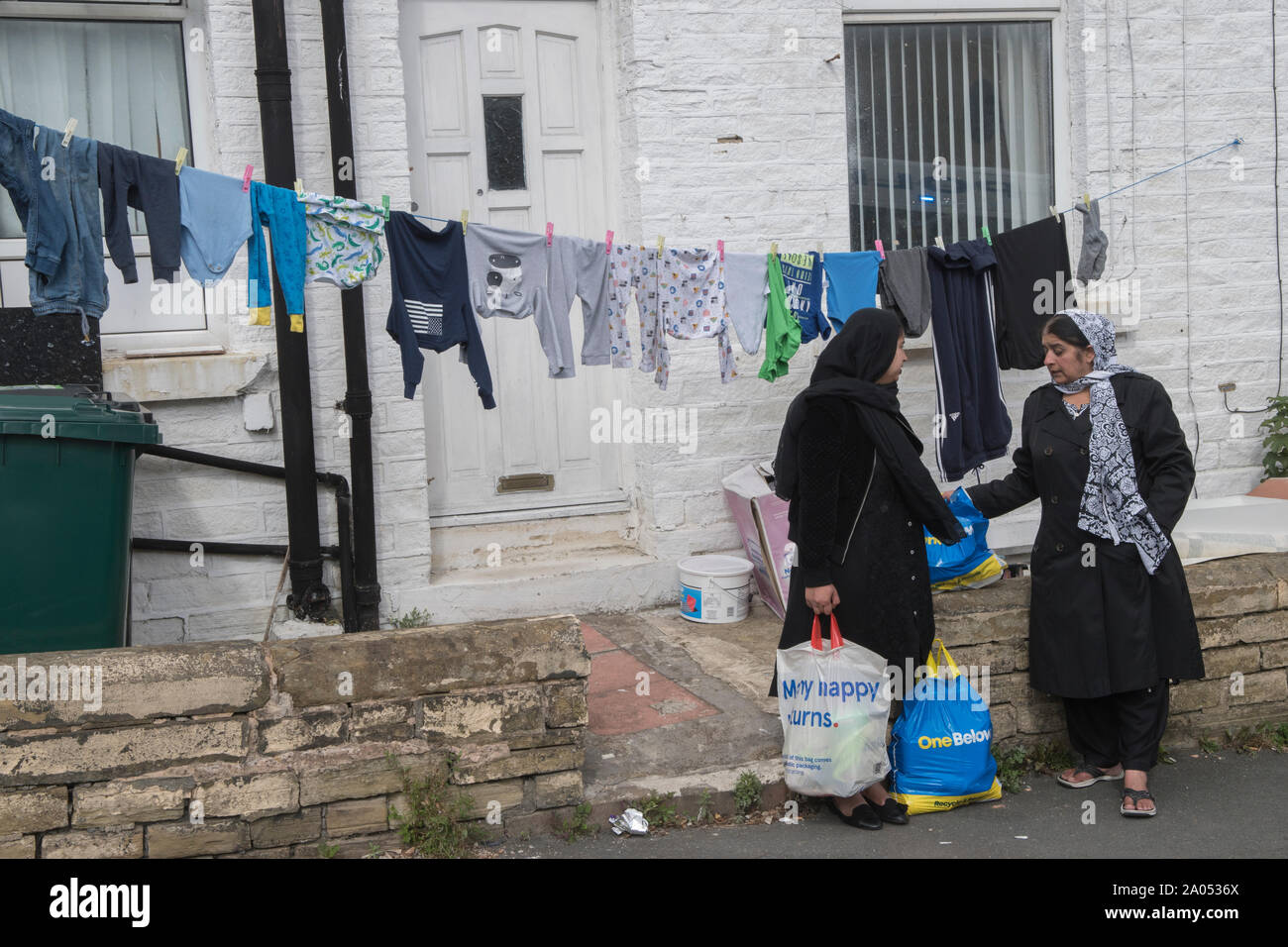 Muslimische Frauen Bradford Yorkshire 2019, 2010er Jahre Großbritannien. Frauen, die auf der Straße plaudern, tragen traditionelle schwarze Gewänder, genannt Abaya. Das wird in der Öffentlichkeit getragen. Waschen hängt an einer Wäscheleine im Vorgarten. HOMER SYKES Stockfoto