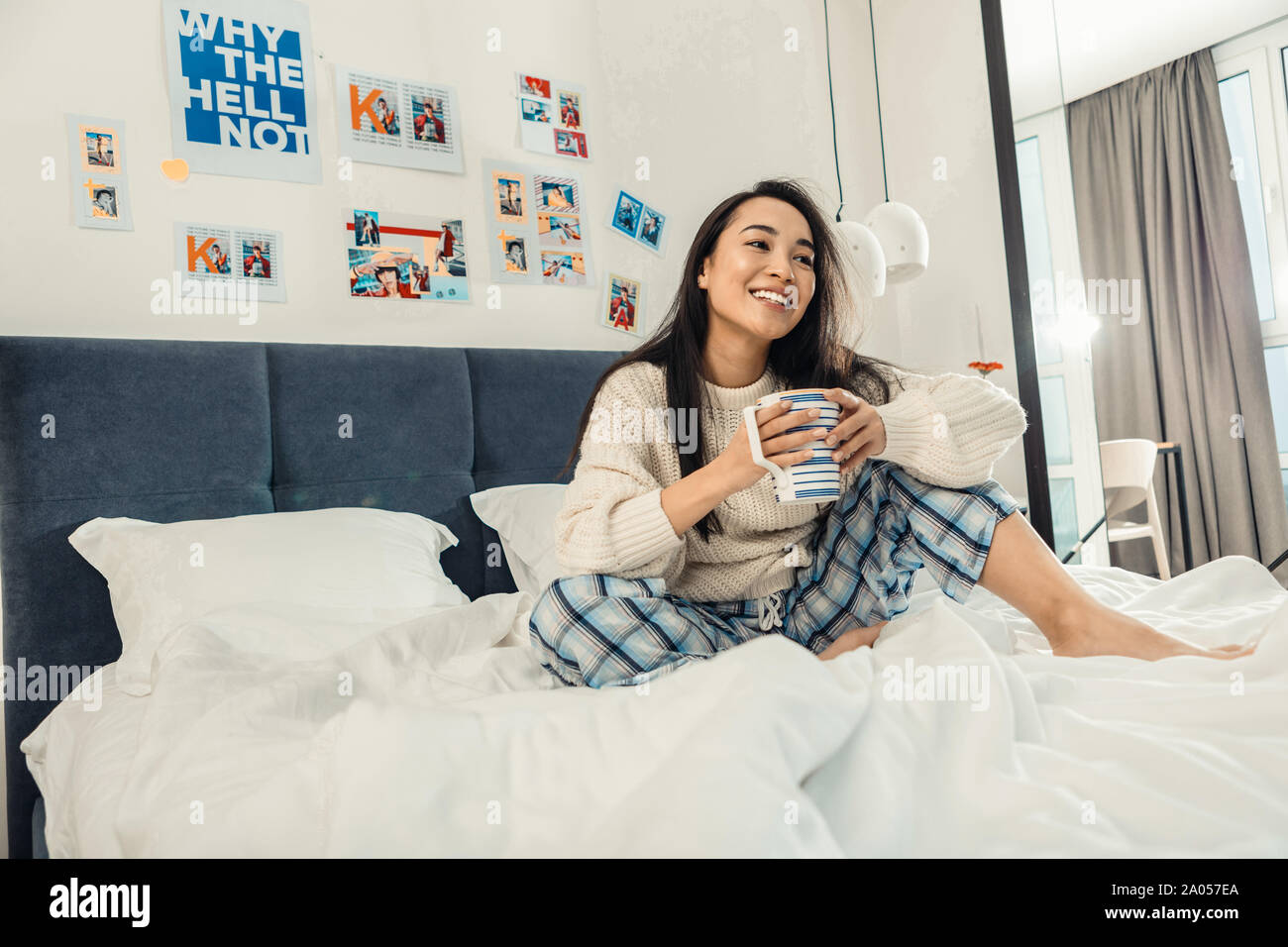Fröhliches Mädchen mit einem toothy Lächeln allein in ihrem Bett mit großen Tasse Tee Stockfoto
