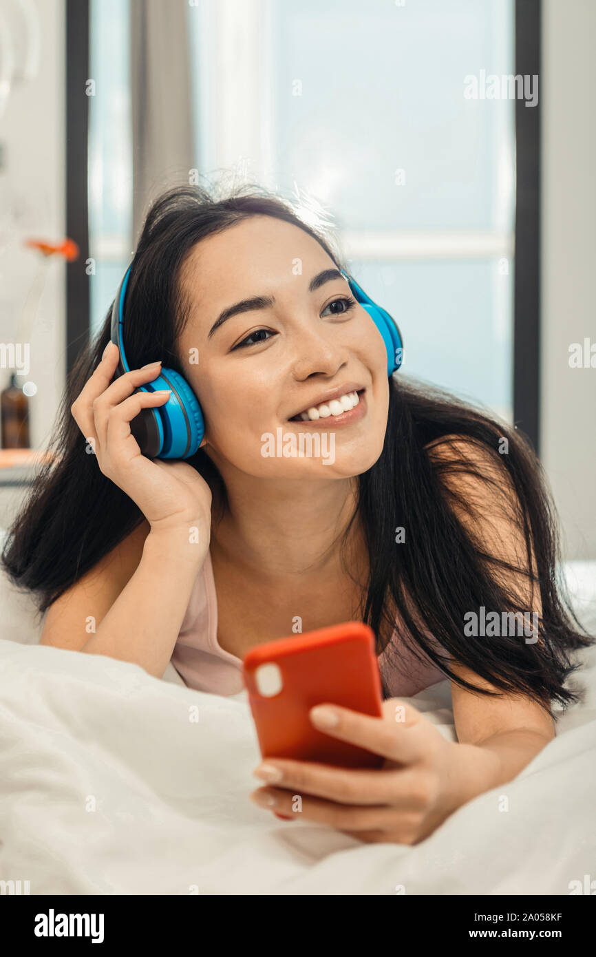 Lächelnde junge Dame liegt in ihrem Bett und Hören von Musik tragen große Kopfhörer Stockfoto