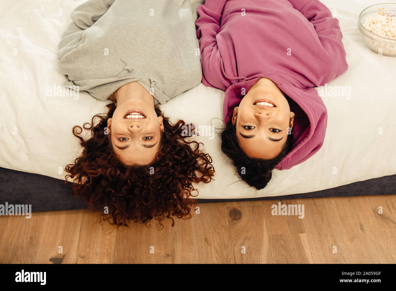 Zwei freundliche junge Damen auf dem Bett liegend mit dem Kopf in der Nähe der Boden Stockfoto