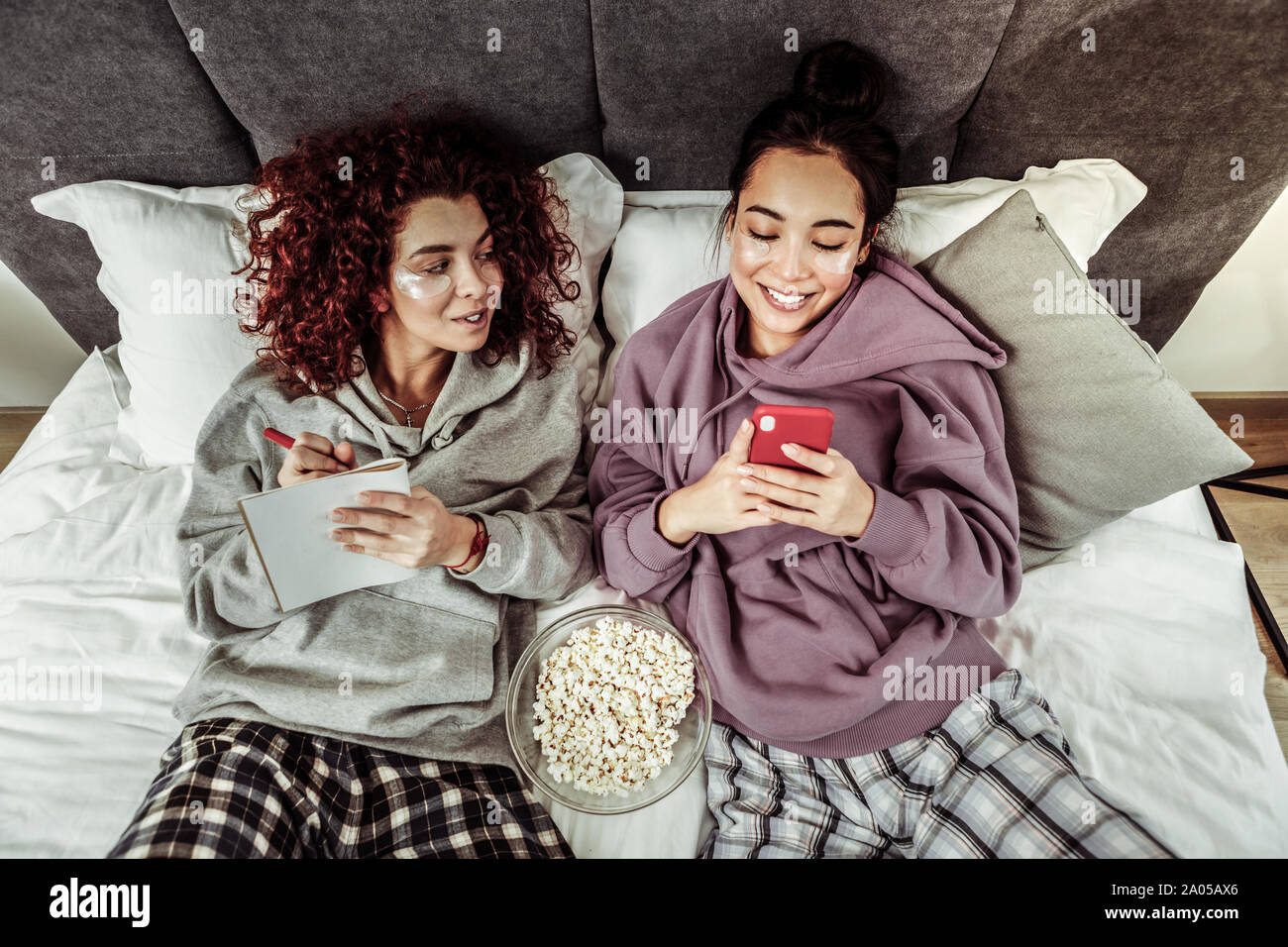 Hübsche junge Frauen sprechen und essen Popcorn im Bett lag, Stockfoto