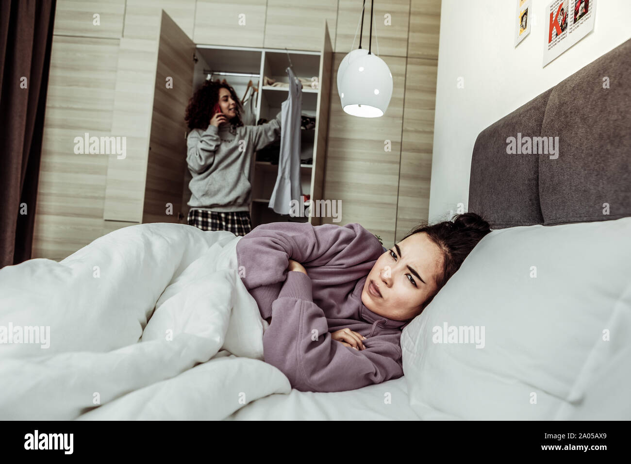 Mürrische junge Dame Kreuzung Arme auf der Brust im Bett vor ihr Mitbewohner liegen Stockfoto