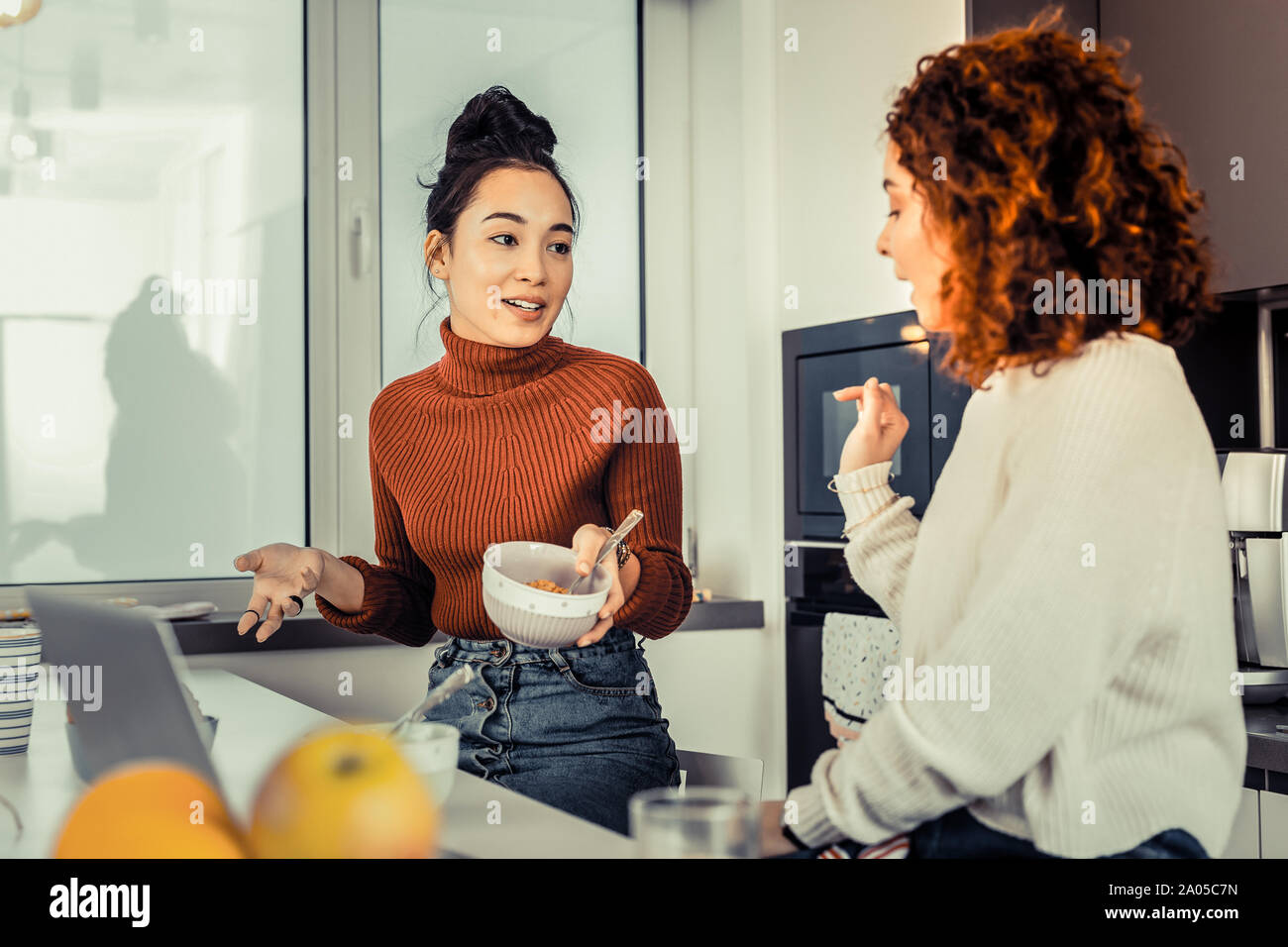 Hübsche junge Frauen in der Küche sitzen und diskutieren Ihre Nachrichten beim Frühstück Stockfoto