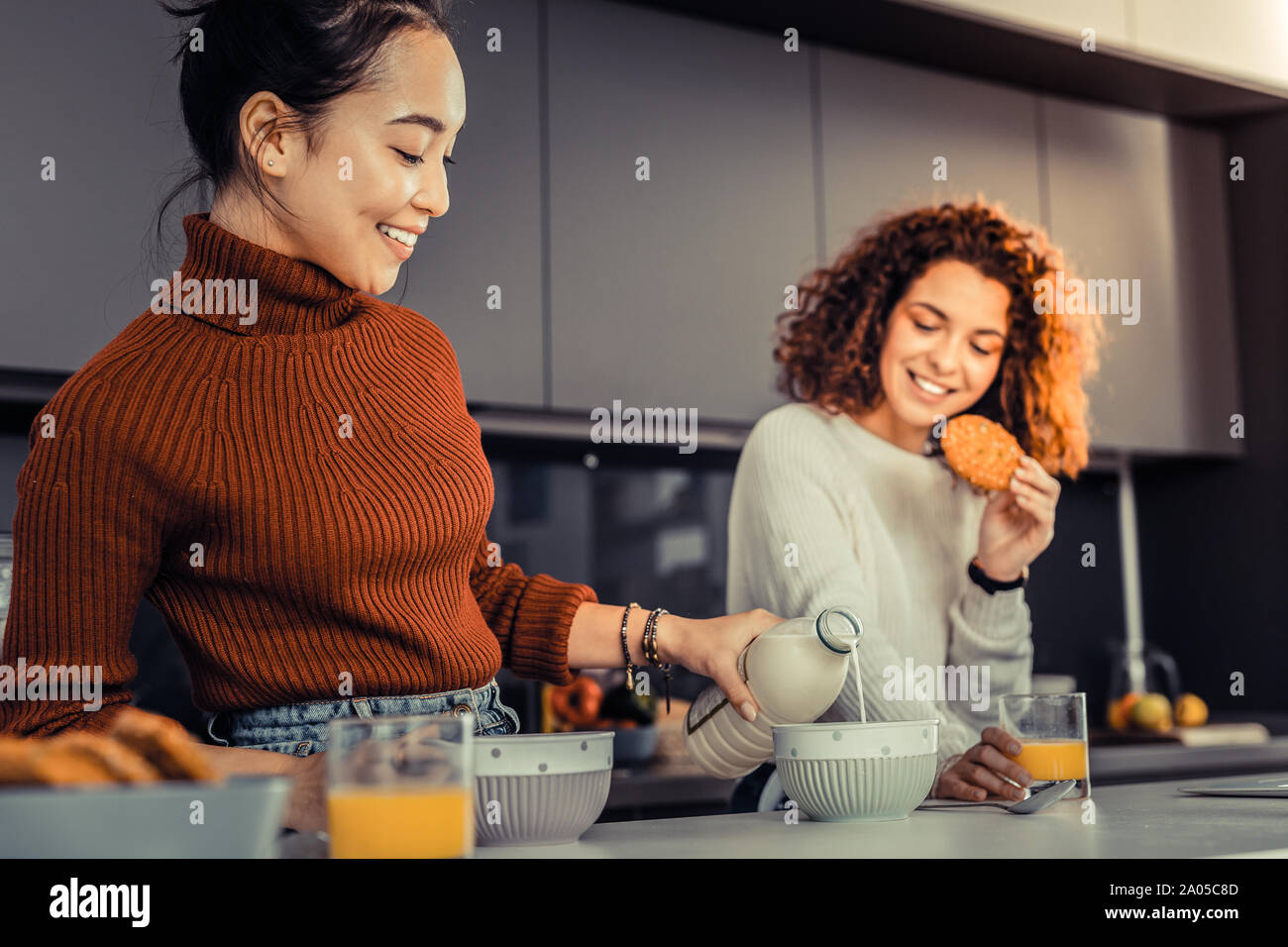 Lächelnden jungen Frau Hinzufügen etwas Milch zu Ihr und Ihren Mitbewohnern Frühstück Stockfoto