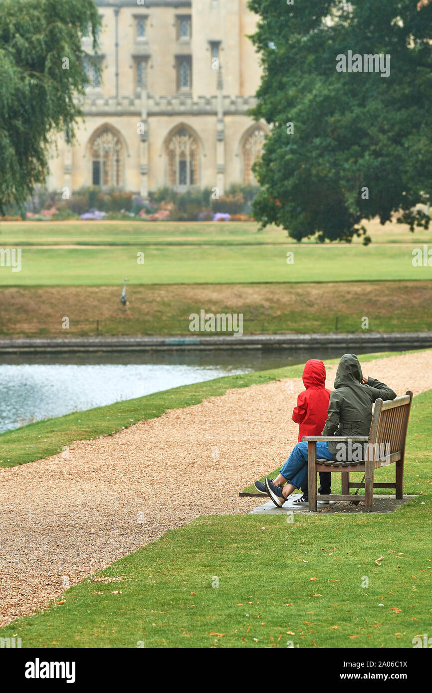 Mutter und Tochter an einer Bank neben dem Fluss Cam am Trinity College der Universität Cambridge, England, mit St John's College im Hintergrund. Stockfoto