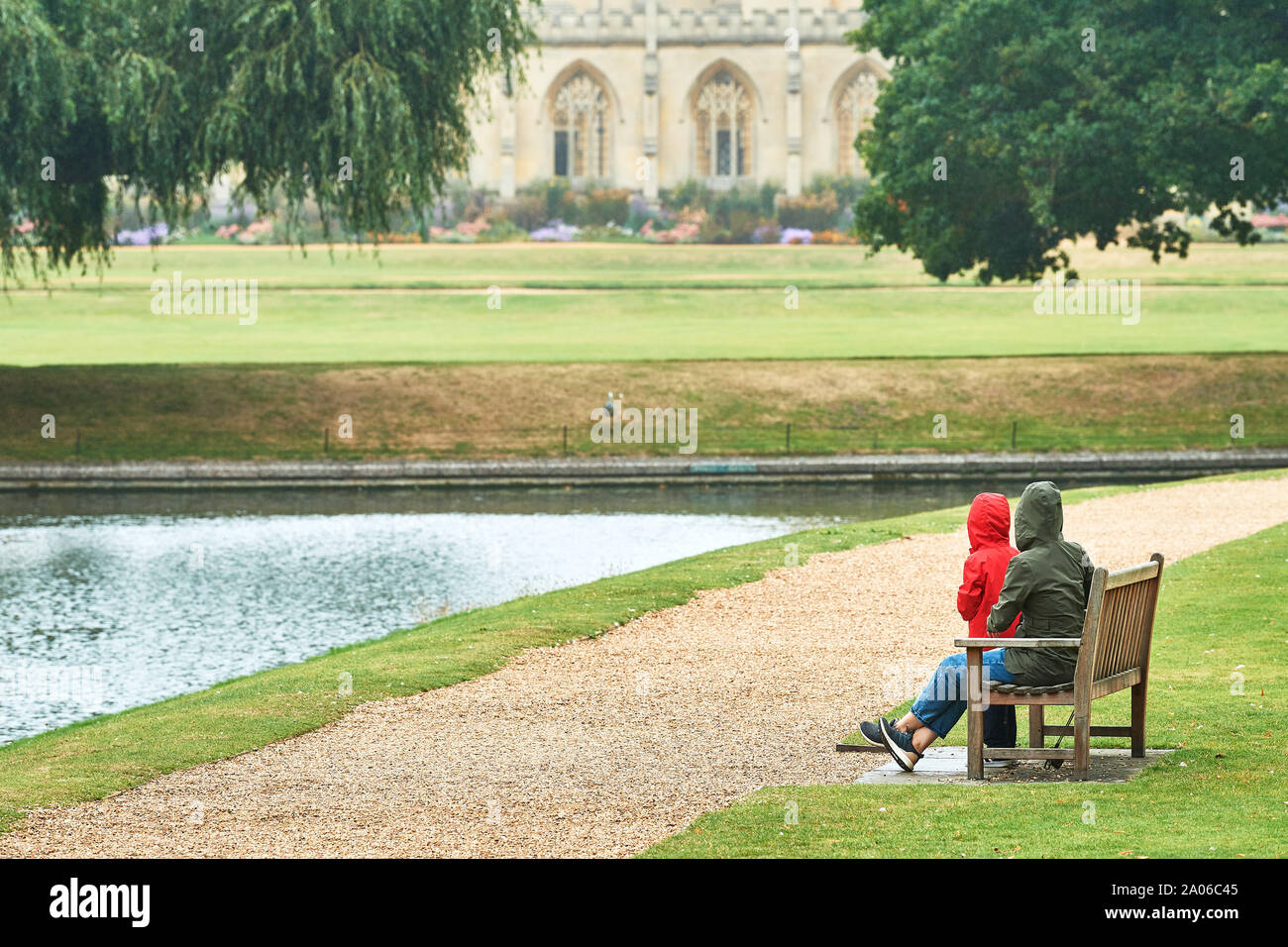 Mutter und Tochter an einer Bank neben dem Fluss Cam am Trinity College der Universität Cambridge, England, mit St John's College im Hintergrund. Stockfoto