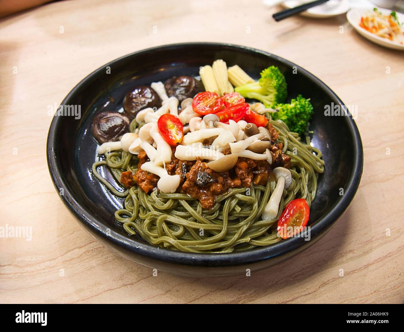 Vegetarische Matcha/grüner Tee Nudeln mit Gemüse und herzhaften tofu Sauce in schwarz Schüssel auf hölzernen Tisch Stockfoto
