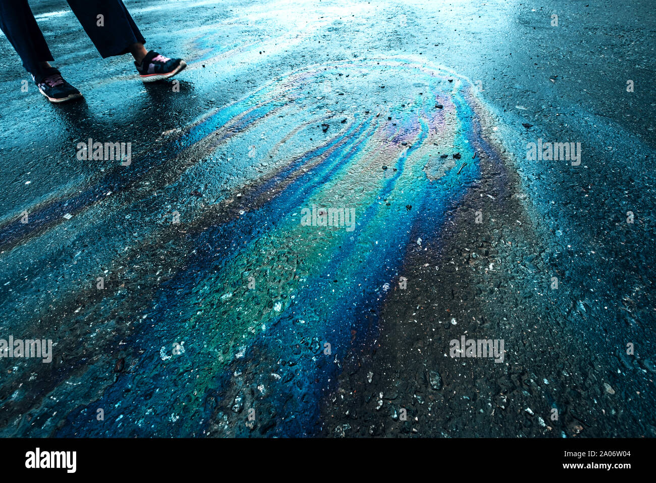Rainbow Flecken auf dem Asphalt. Benzin Streifen, Motor undicht auf nasser Fahrbahn Konzept. Mann quer durch Farbe ölteppiche Outdoor. Kraftstoff Flecken Stockfoto