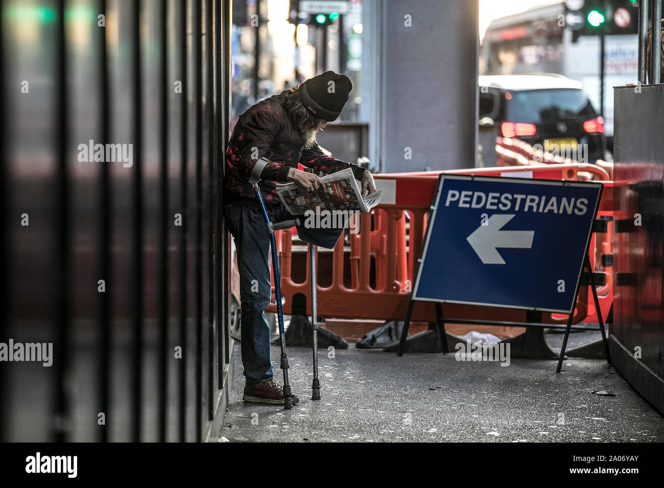 Homelessman stehend auf seinem nur Bein von Krücken, während Sie die Zeitung lesen unterstützt und das Rauchen einer Zigarette auf den Straßen von London, England, Großbritannien Stockfoto
