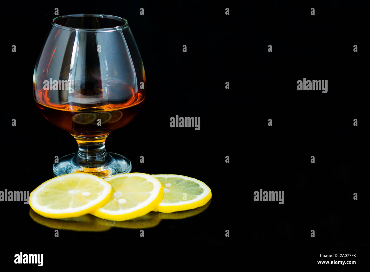 Glas Cognac und Zitronenscheiben auf schwarzem Hintergrund isoliert. Platz kopieren Stockfoto