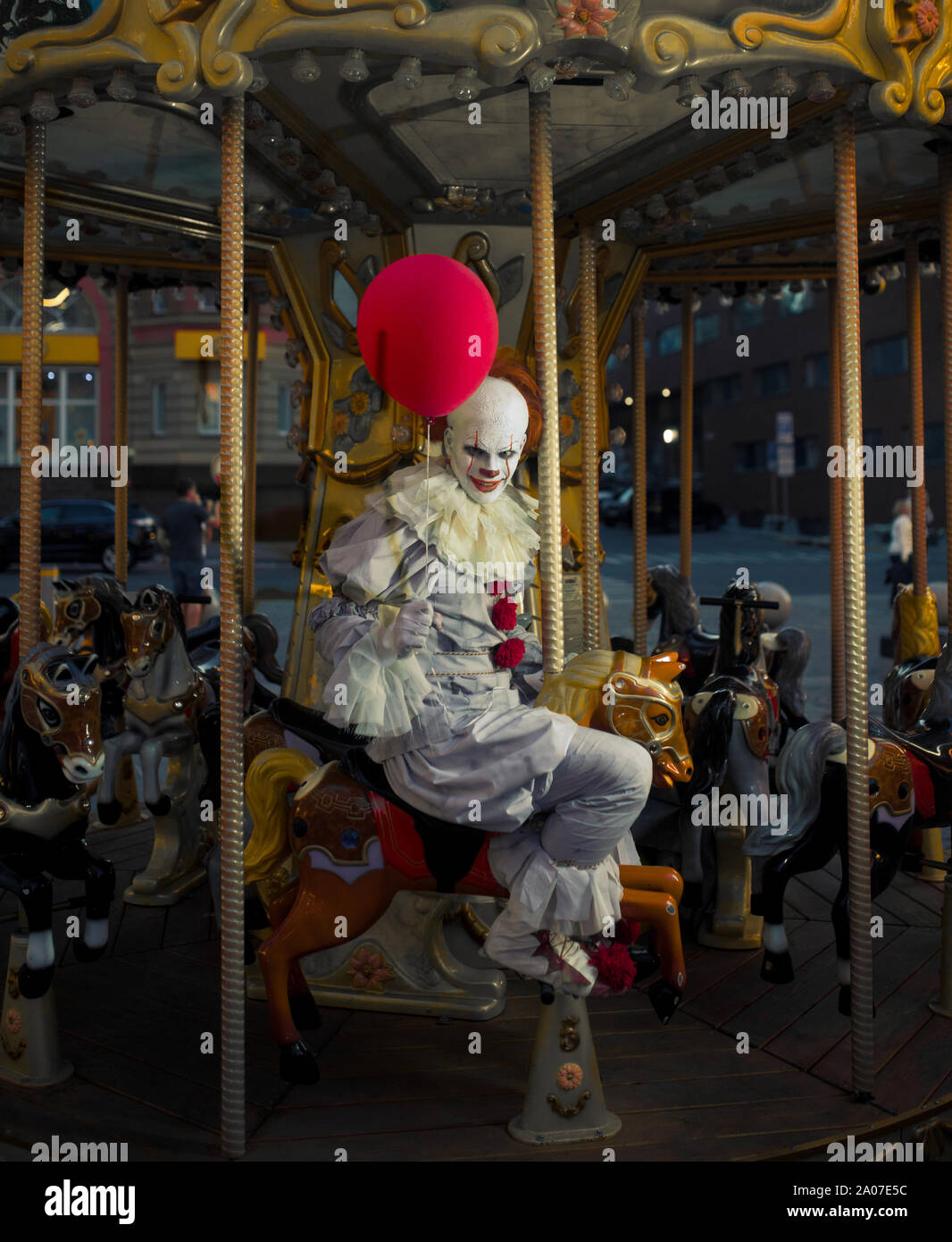 Ein Mann in das Bild eines Clowns reitet ein Karussell auf ein Pferd mit einem roten Ballon in der Hand. Stockfoto