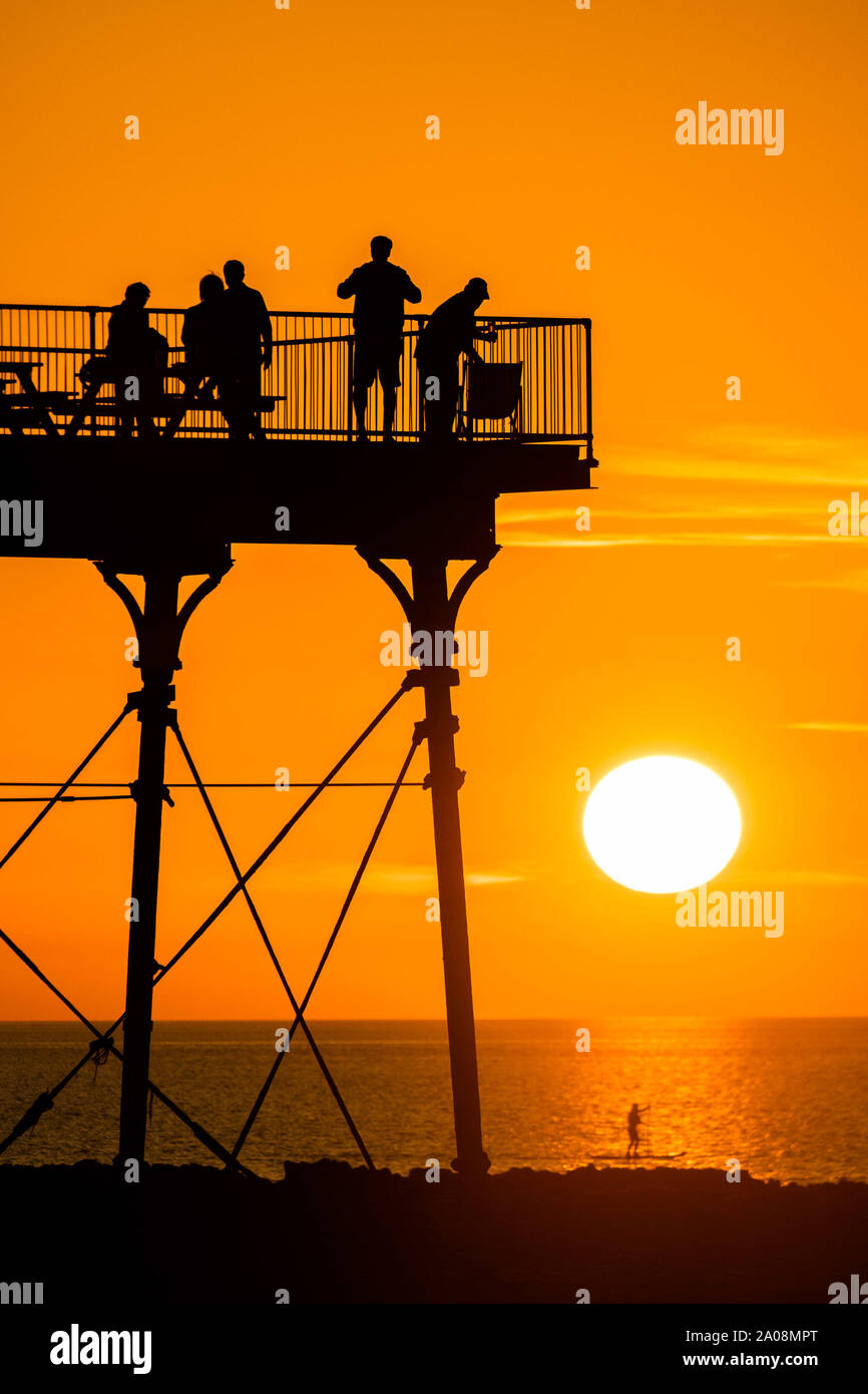 Aberystwyth Wales UK, Donnerstag, den 19. September 2019 die Sonne herrlich Einstellung über die Cardigan Bay Silhouetten peopke genießen einen freien Drink auf der Pier am Ende eines Tages des ungebrochenen klaren blauen Himmel und warmen September Sonnenschein in Aberystwyth, West Wales. Als 'Indian Summer' mini Hitzewelle weiterhin über die südlichen Teile der britischen Photo credit Keith Morris/Alamy leben Nachrichten Stockfoto