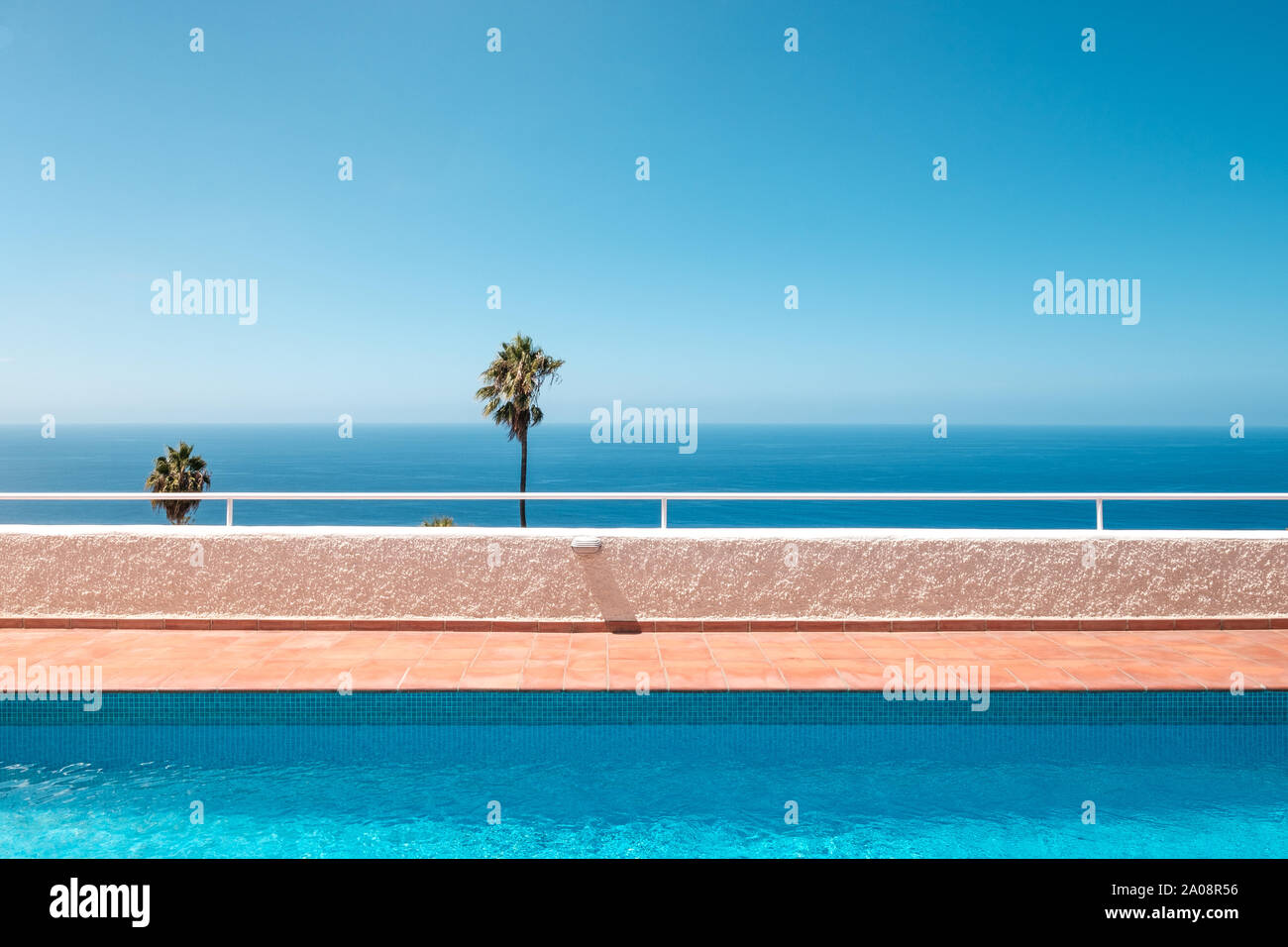 Außenpool mit Blick auf das Meer, Palmen und strahlend blauer Himmel Stockfoto