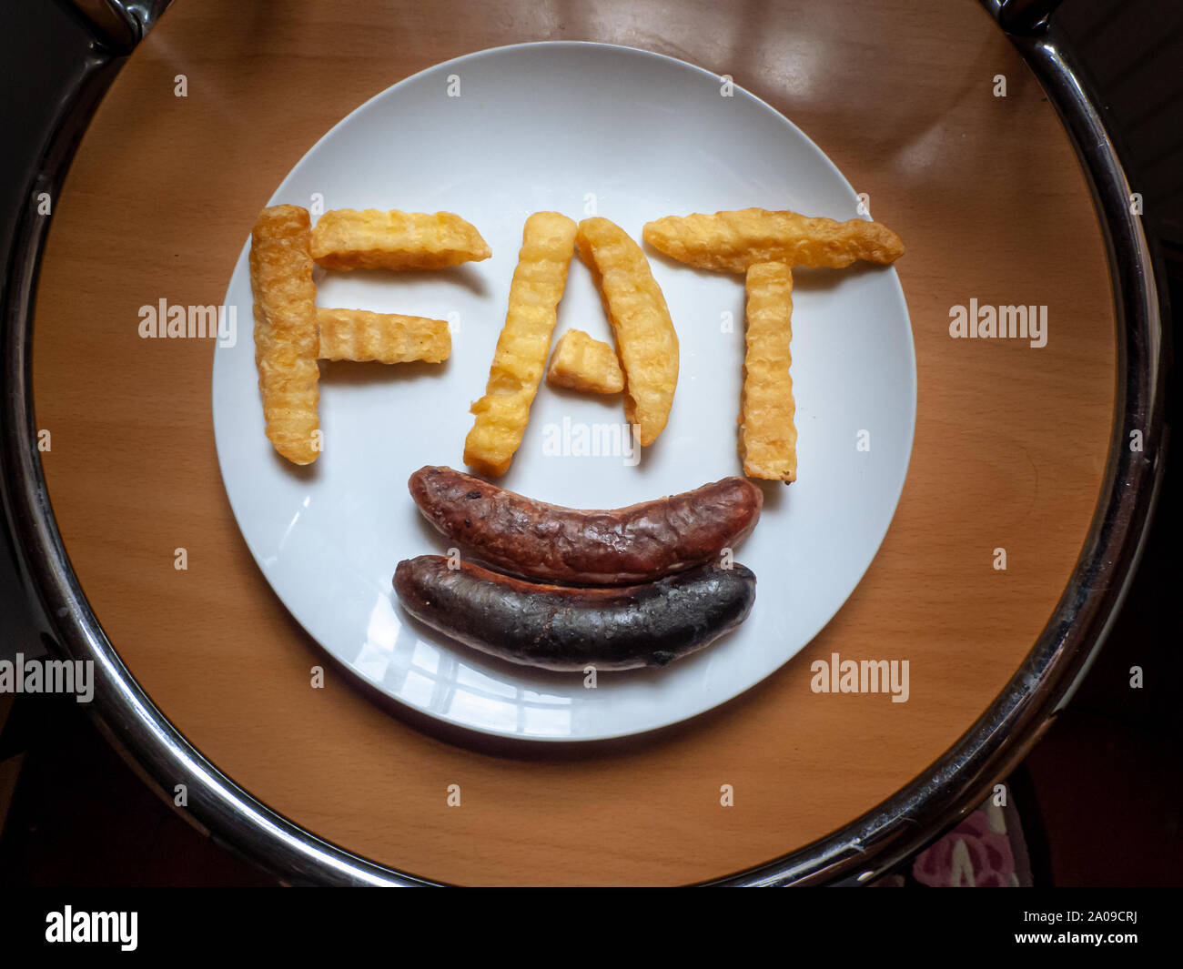 Das Wort "Fett" mit CRINKLE-cut-Chips mit gebratenen Würstchen geschrieben auf einer weißen Platte Stockfoto