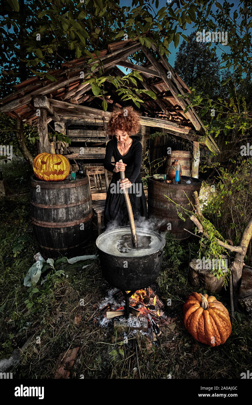 Alte Hexe brauen tödlichen Trank für Halloween in einen gusseisernen Topf Stockfoto