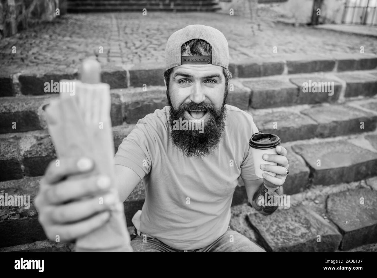Mahlzeit, schmeckt Recht. Bärtiger Mann essen ungesundes Essen während der Ruhe- und Essenspause. Hipster essen Hot Dog Essen auf Treppen im Freien. Kaukasische Kerl genießen essen Essen zum Mitnehmen. Stockfoto