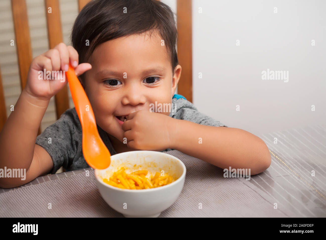 Eine nette junge Zicklein an einem Tisch sitzen mit ein eifriger Mimik und Löffel in der Hand, bereit zum Start Essen auf seinem eigenen. Stockfoto