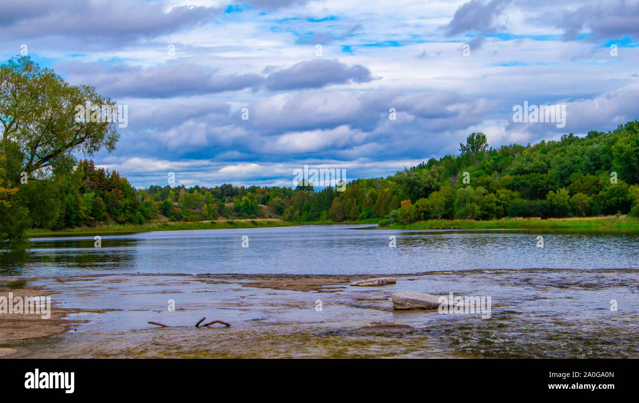 Die reflektierte Oberfläche eines Flusses erstreckt sich auf einem Hintergrund von Waldbäumen und bewölktem Himmel. Stockfoto