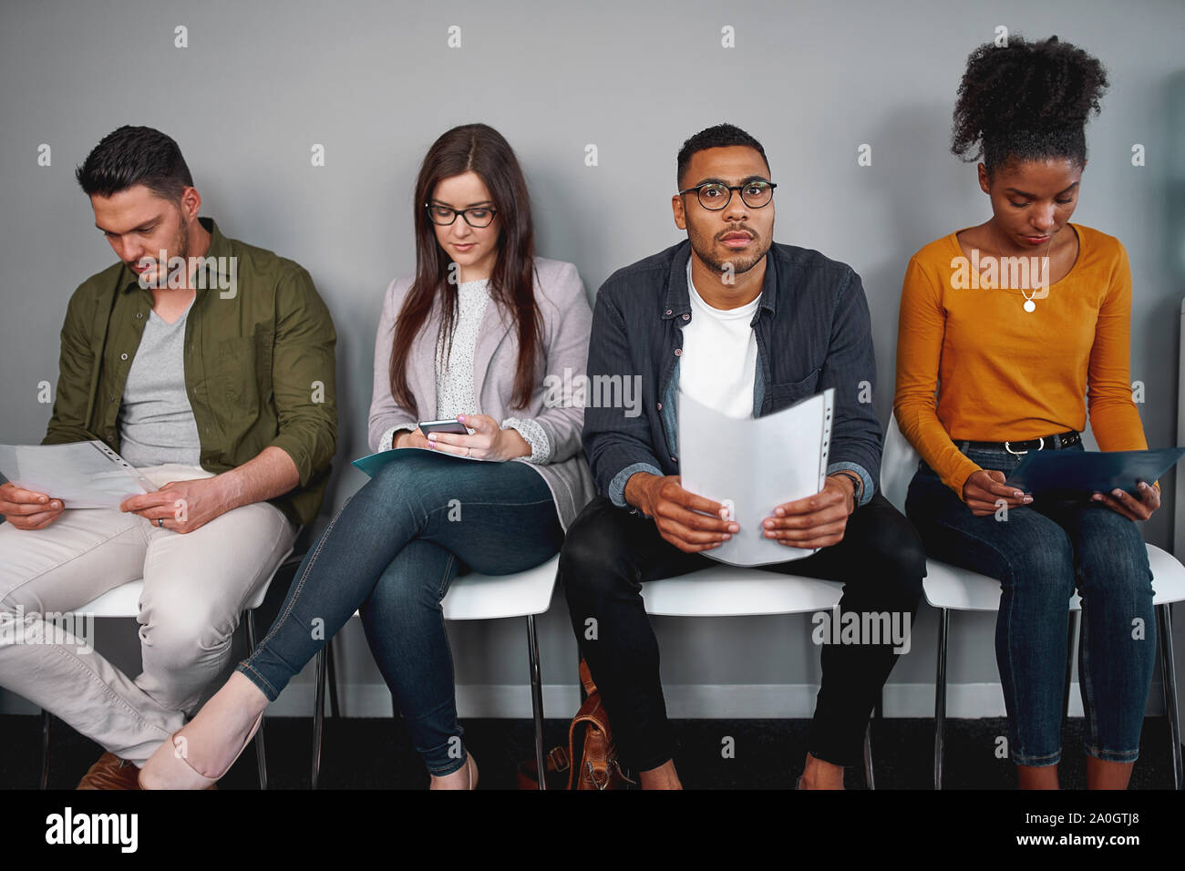 Gruppe der Multirassischen jungen Kandidaten warten auf Interview sitzen auf Stuhl ihre Lebensläufe Holding Stockfoto