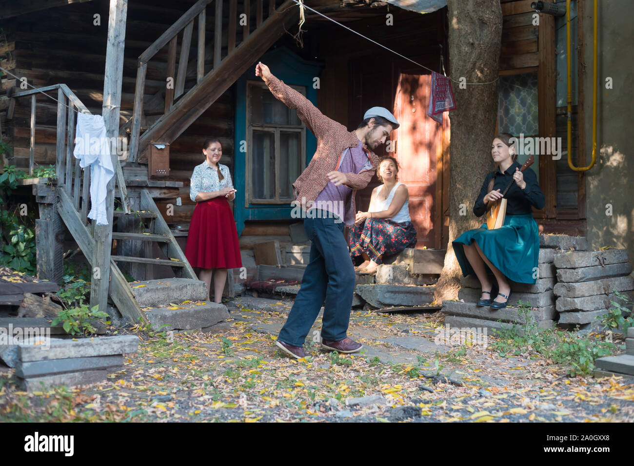 Ein Mann tanzen russischen Volkstanz - Frauen sitzen auf der Treppe in der Nähe des Country House und beobachten ihn und Händeklatschen - eine Frau spielen Balalaika Stockfoto