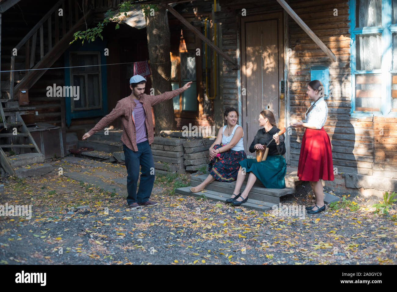 Ein Mann tanzen Russischer Tanz - Frauen sitzen auf der Treppe in der Nähe des Country House und miteinander sprechen - eine Frau spielen Balalaika Stockfoto