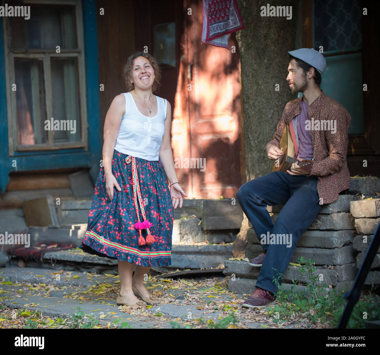 Eine lächelnde Frau stand in der Nähe des Country House und ein Mann spielt Balalaika Stockfoto