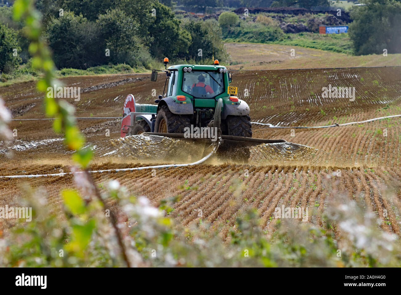 Gülle verbreiten sich in Fortschritt durch ein langes Rohr aus der Farm ein John Deere Traktor in einem Feld in der Nähe von Felder Farm in der Nähe von Sandbach in Cheshire. Stockfoto