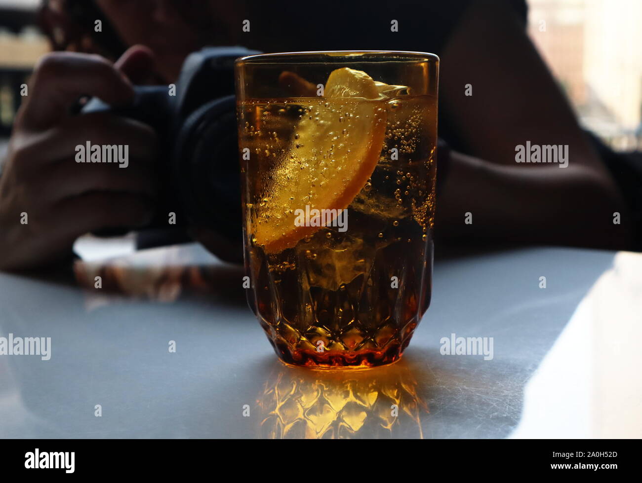 Fotografin mit Canon DSLR-Kamera fotografieren golden Glas Wasser mit Kohlensäure mit zitronenscheibe Stockfoto