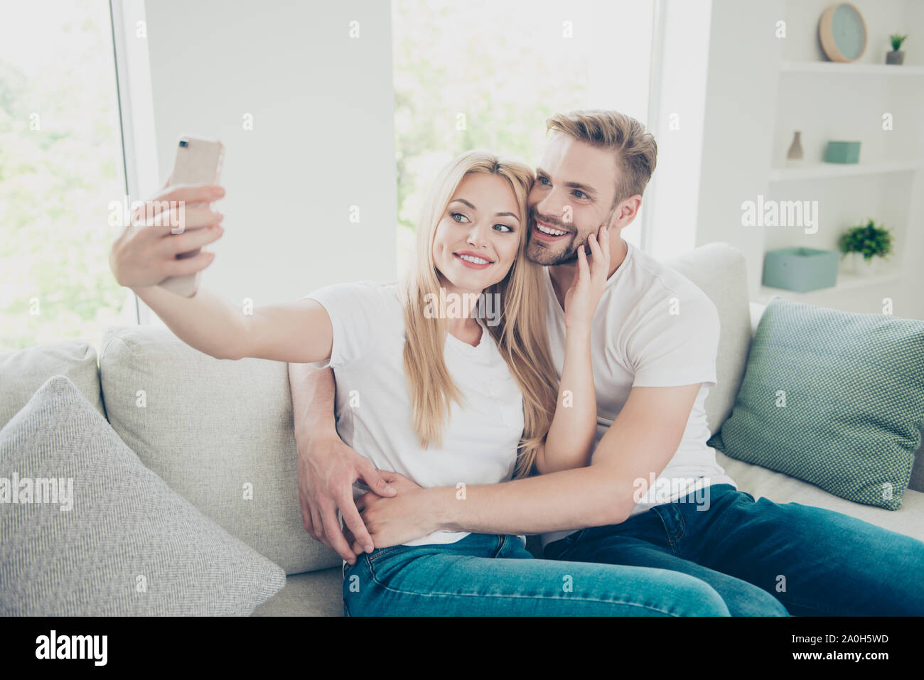 Schöne attraktive schön schön süß Heiter adorable stilvolle trendige Paar in lockeren weißen T-Shirts und Jeans zu Hause, sitzen auf den divan, Sel Stockfoto