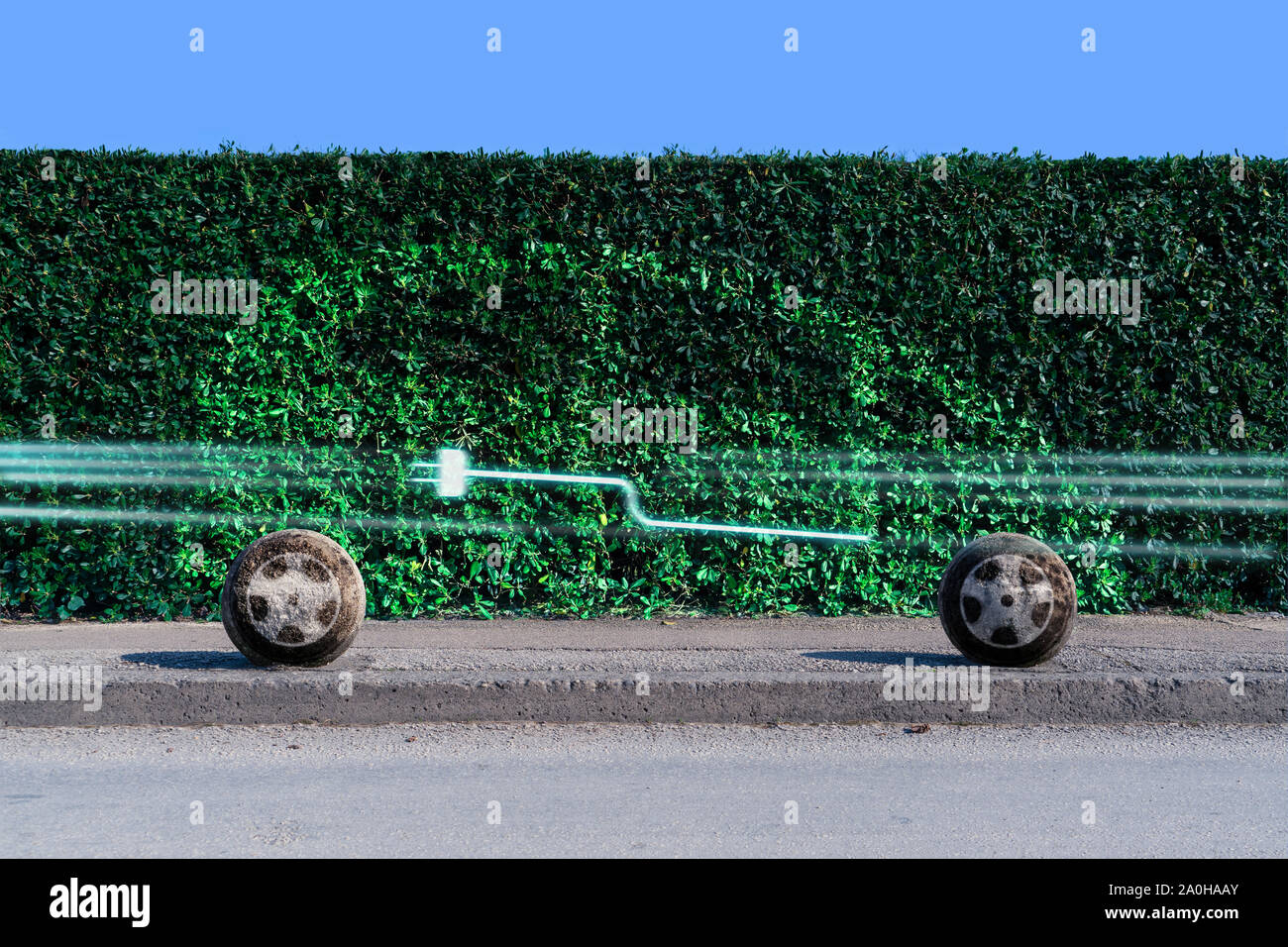Silhouette eines Elektroautos auf einer Hecke auf einer Straße der Stadt. Die Lichter der vorbeifahrenden Autos bilden ein ladesymbol. Stockfoto