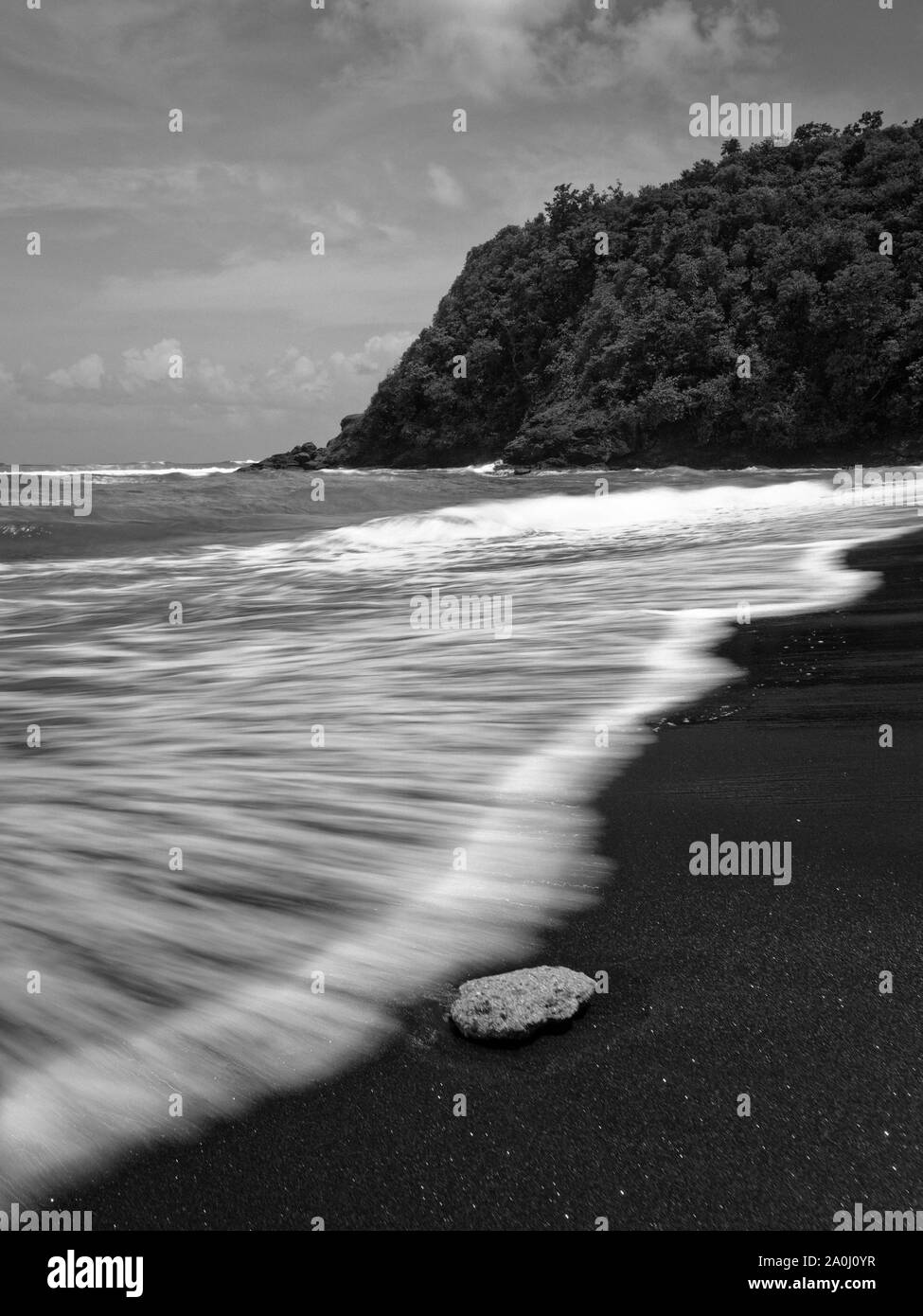 Schöne Wellen auf einem dunklen Sandstrand auf Martinique. Stockfoto