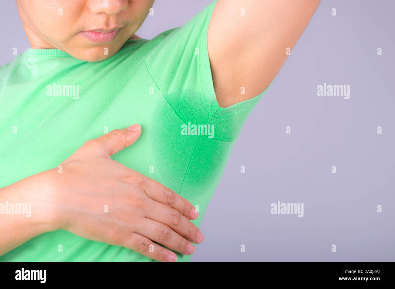 Close-up junge Frauen mit Hyperhidrose schwitzen. Junge Frau mit Schweiß Flecken auf Ihrer Kleidung vor grauem Hintergrund. Healthcare Konzept. Stockfoto