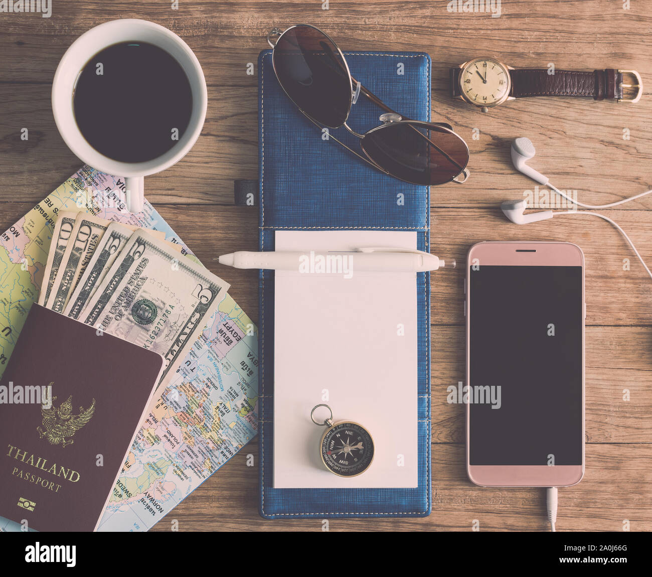 Notizbuch, Stift, Sonnenbrille, Kaffeetasse, Pass, Geld, Handy, Ohrhörer, Karte, Armbanduhr und Kompass auf Holzbrett. Travel Concept. Stockfoto