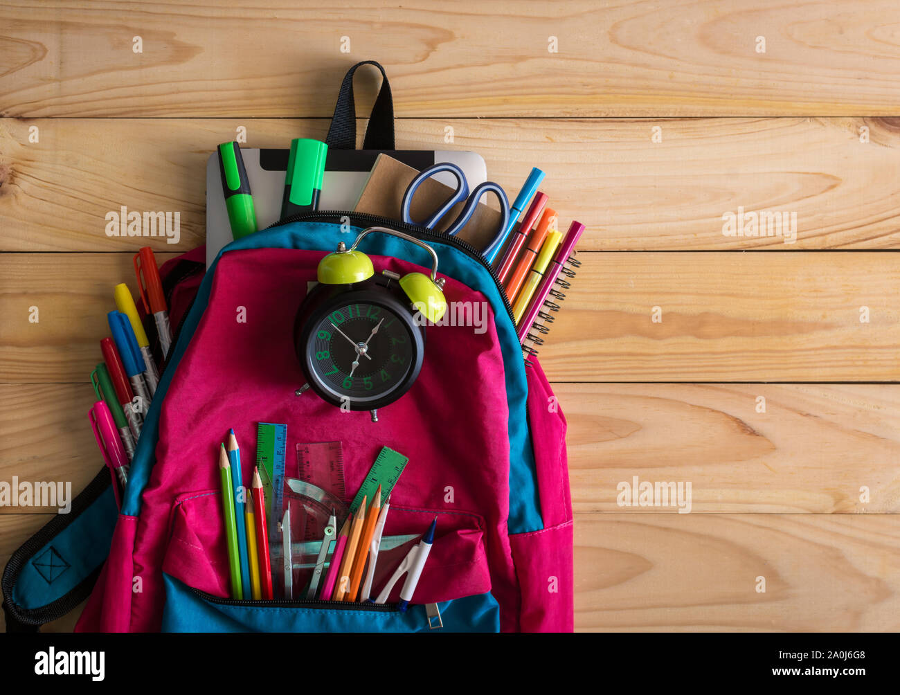 Schule Rucksack mit Schulmaterial und Uhr auf hölzernen Tisch Hintergrund. Zurück zum Konzept der Schule. Stockfoto