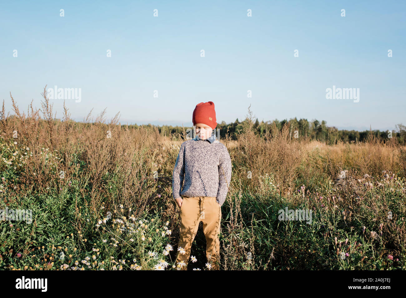 Junge Junge stand in einem Feld in seinen Taschen denken mit seinen Händen Stockfoto