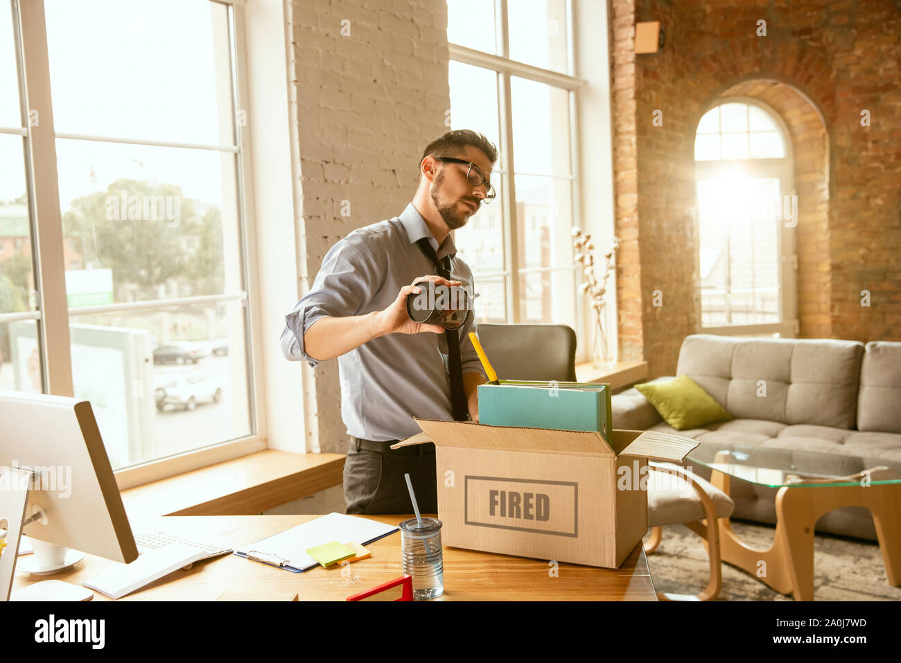 Junge Unternehmer abgefeuert, wütend aussieht. Hat sein Büro Sachen zu packen und Arbeitsplatz für neue Arbeitnehmer zu verlassen. Probleme im Beruf, Stress, Arbeitslosigkeit, ein neuer Weg des Lebens oder am Ende der Karriere. Stockfoto