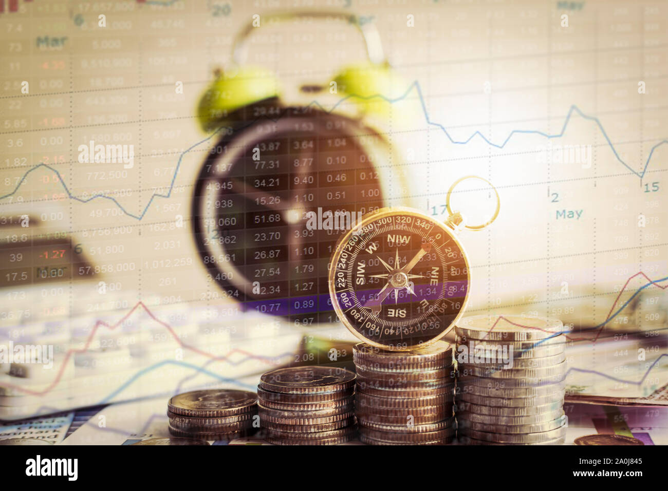 Close up Kompass auf Stapel von Münzen mit Wecker und Börse Grafik Informationen. Investitionen und Wirtschaft Konzept. Stockfoto